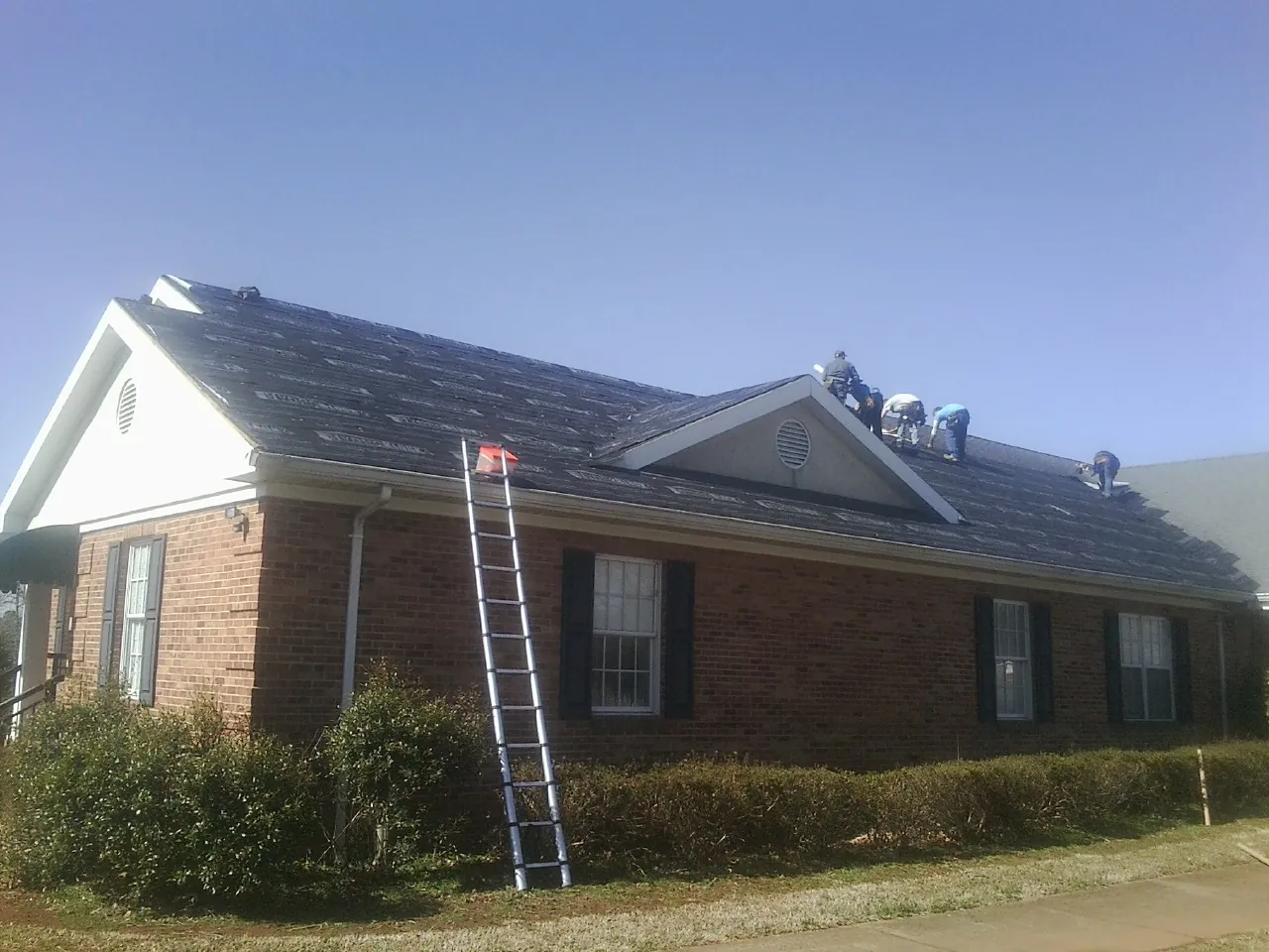 Crew tearing shingles off a brick ranch roof with a ladder set — Emergency Roof Repair work by our crew in Big Clifty