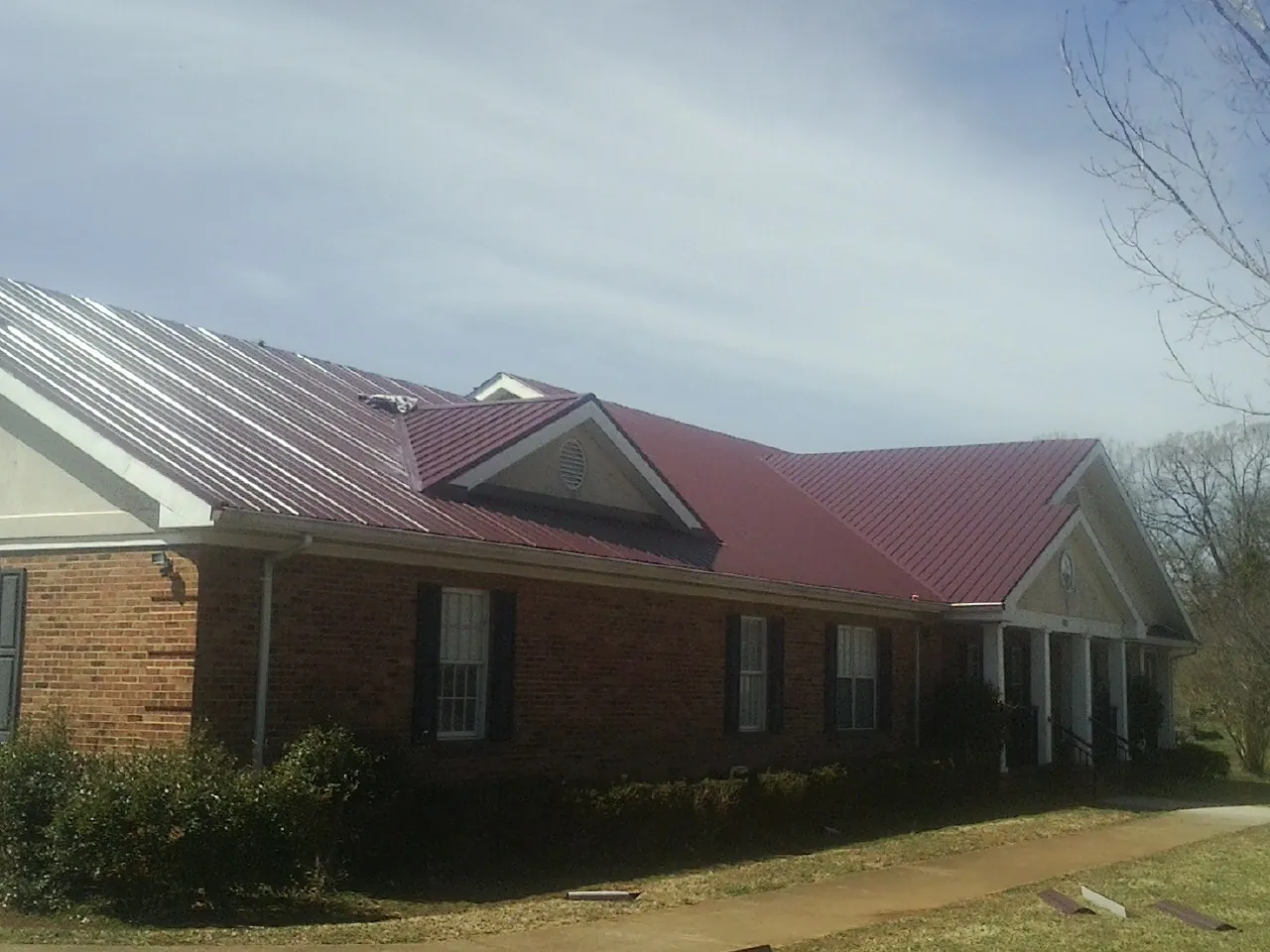 Red metal roof with gabled entries on a long brick building, from a Hail Damage Roof Repair job in Big Clifty