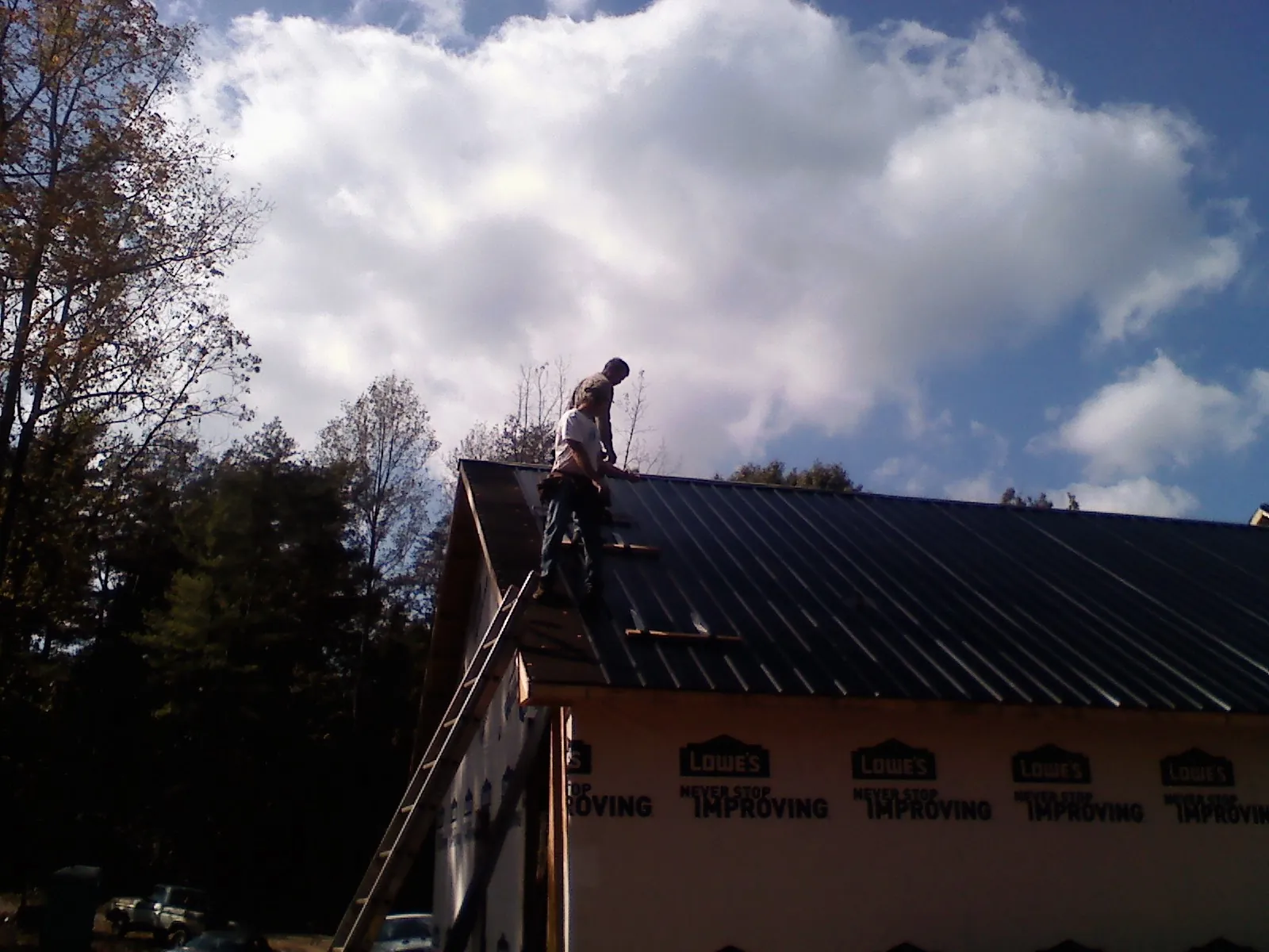 Roofer fastening dark metal panels high against a cloudy sky, from a Roof Inspection job in Big Clifty