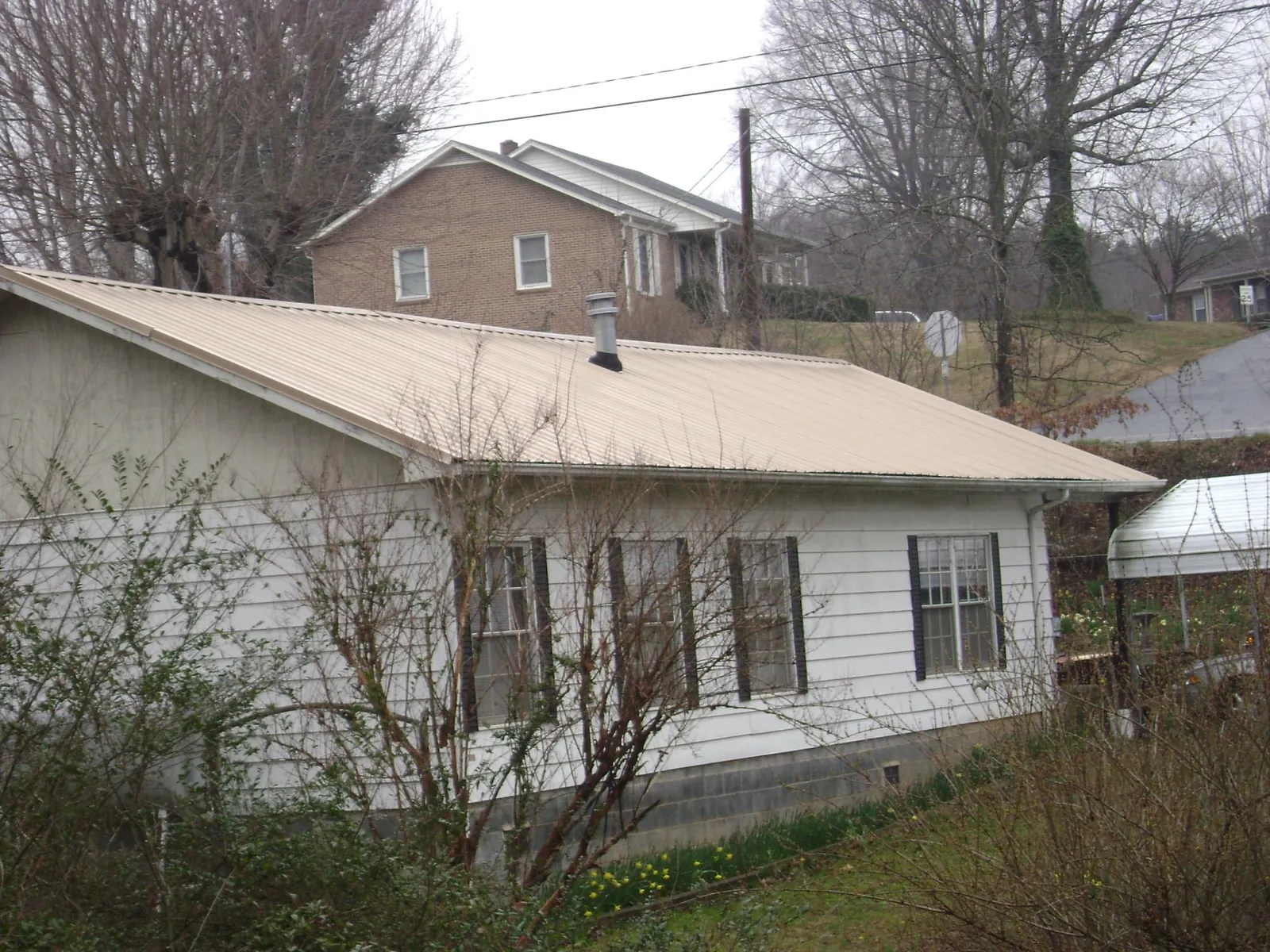 Tan metal roof on a white sided house set into a hillside — Commercial Roofing by Roofing Brothers in Big Clifty