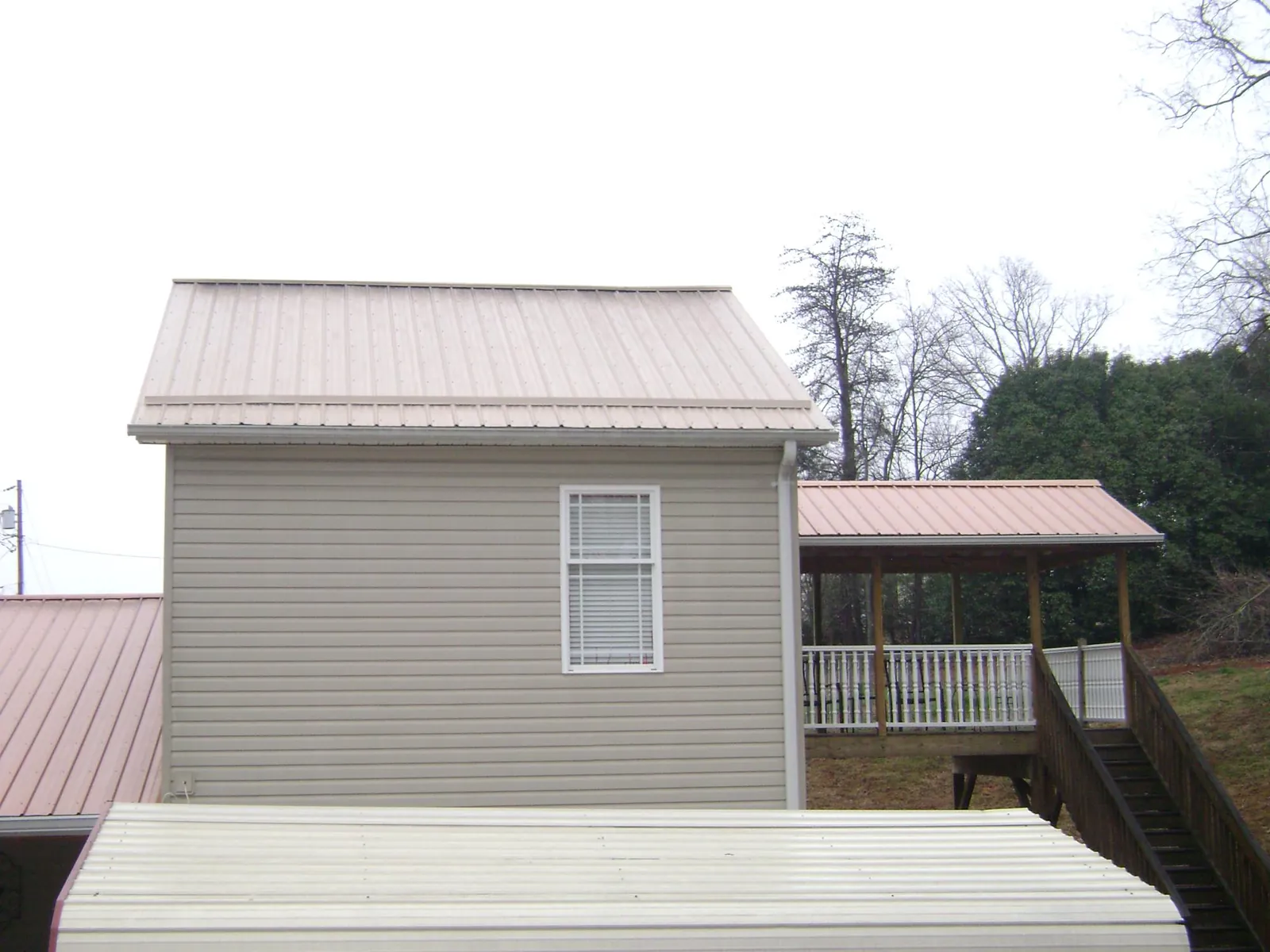 Tan metal roofs on a two story addition and attached porch, from a Roof Replacement job in Big Clifty